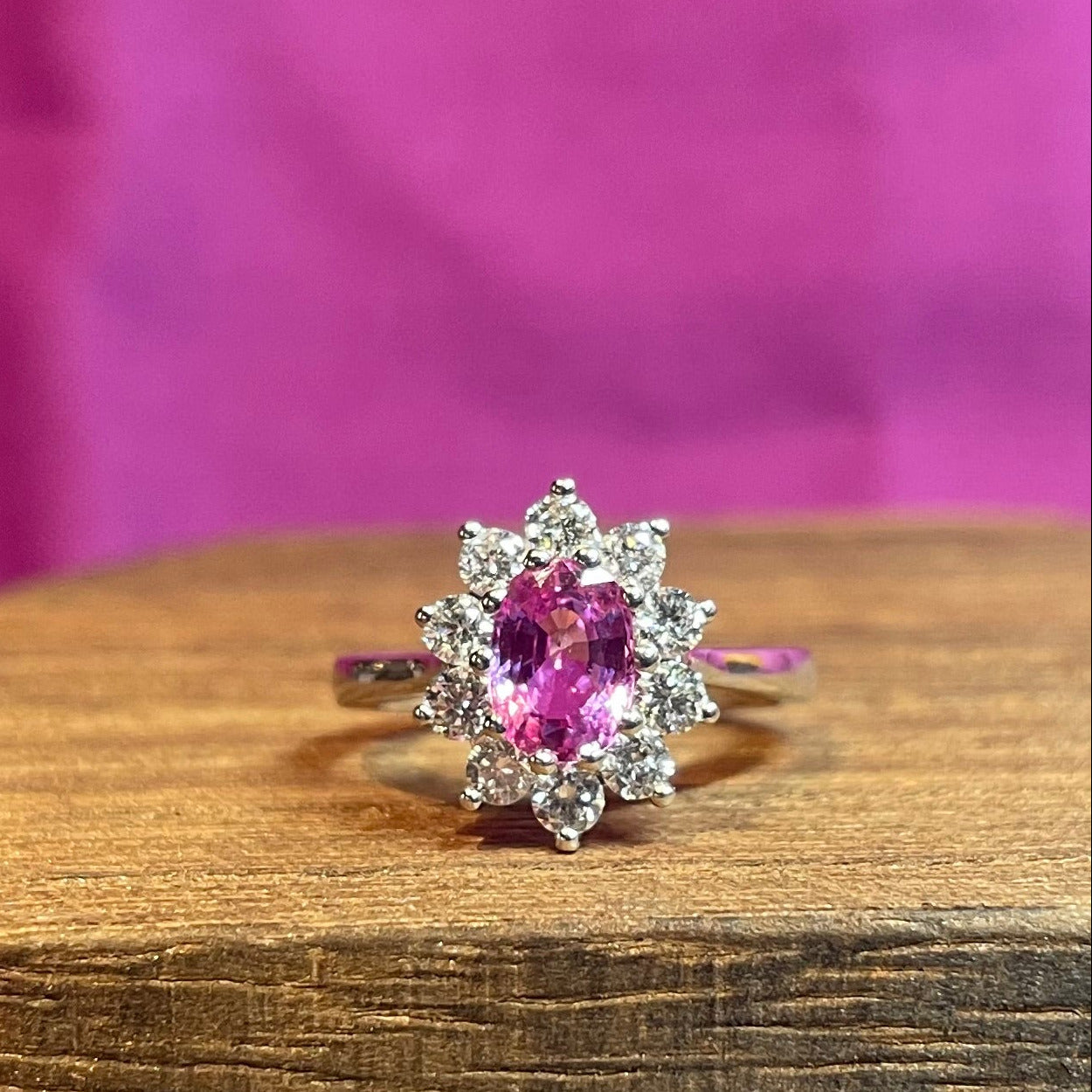 A pink sapphire halo cluster ring from Little Shambles Jewellers on a rustic oak block